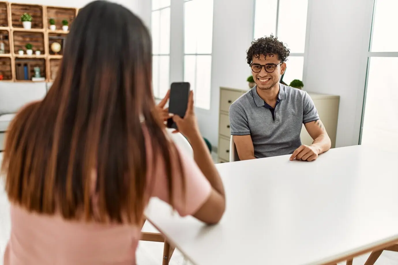 Junge Latina macht zu Hause mit einem Smartphone ein Foto von einem Mann.